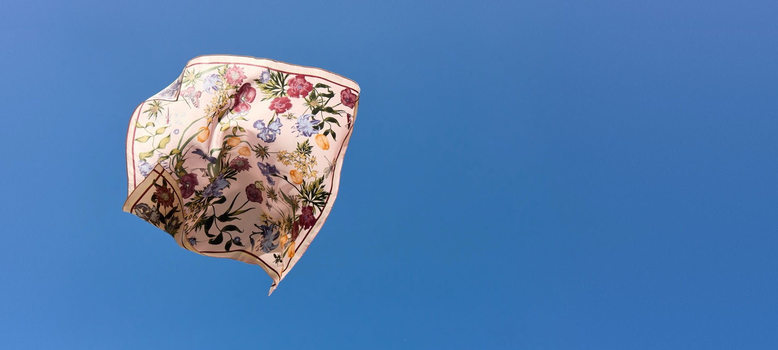 Silketørklæde med blomsterprint i vinden mod en blå himmel